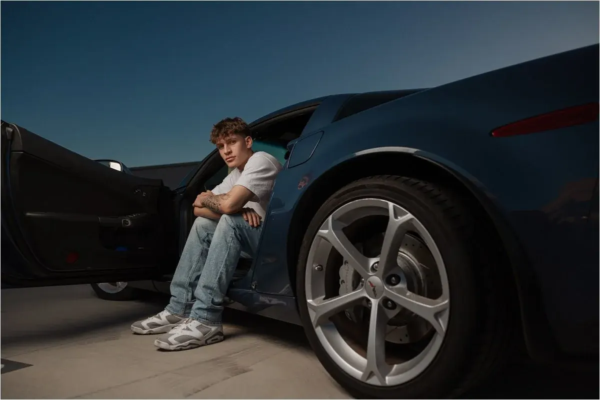 Senior guy sitting beside a sports car at dusk